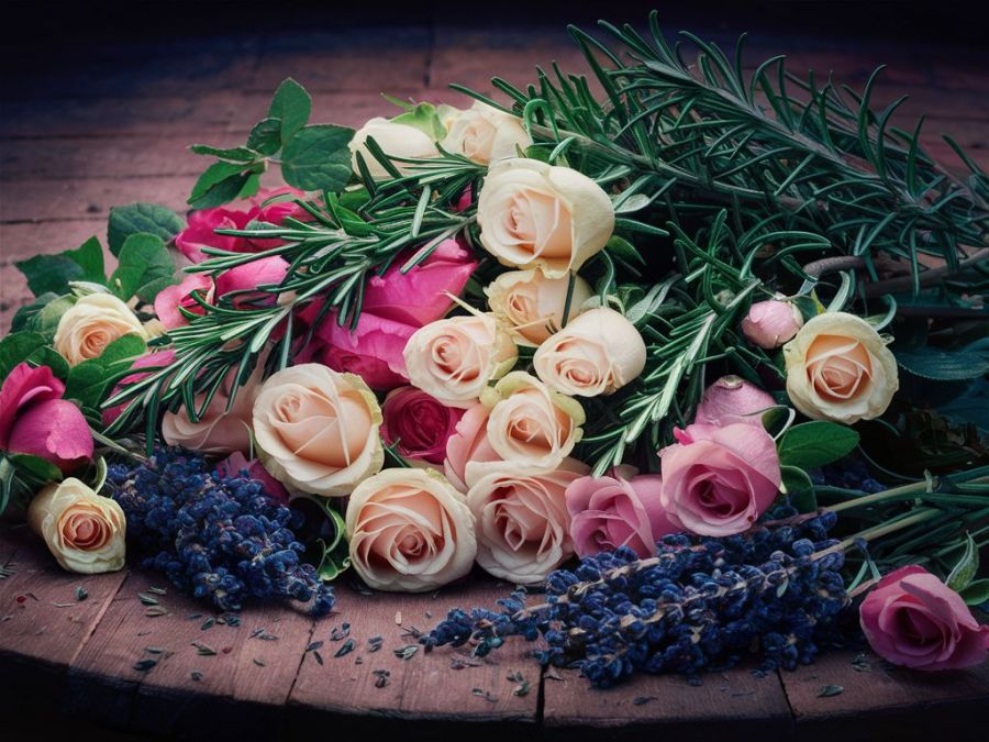 fantasy world image of a pile of roses, rosemary, and lavender, on an old wooden table ready to be used in a fragrant body creme